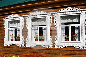 Three windows of a wooden county house decorated by white frames