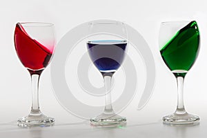 Three wine glasses with colour water spill on white background w