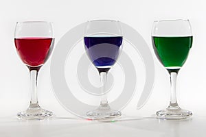 Three wine glasses with colour water spill on white background w
