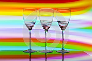 Three wine glasses in a row with a rainbow of color behind them
