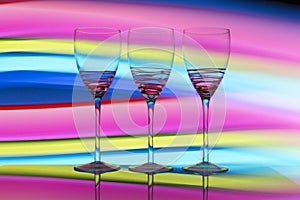 Three wine glasses in a row with a rainbow of color behind them