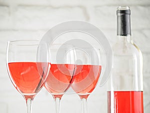 Three wineglass with pink wine and bottle on white brick wall background