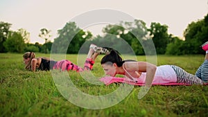 Three women are doing push ups on the grass in the park