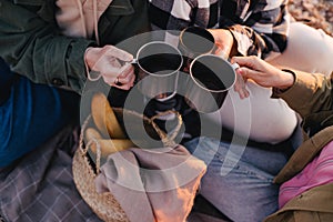 Three women female friends having picnic, drinking hot tea from iron mugs, sitting on beach