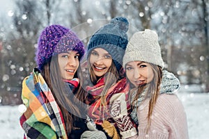 Three women friends outdoors in knitted hats having fun on a snowy cold weather. Group of young female friends outdoors