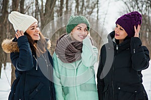 Three women friends outdoors in knitted hats on a snowy cold winter weather.