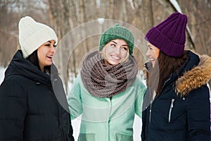 Three women friends outdoors in knitted hats on a snowy cold winter weather.