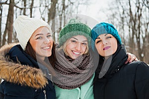 Three women friends outdoors in knitted hats on a snowy cold winter weather.