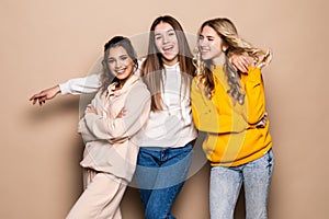 Three women friends standing together on beige background