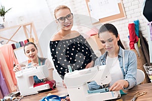 Three women at garment factory. They are sitting behind sewing machines.