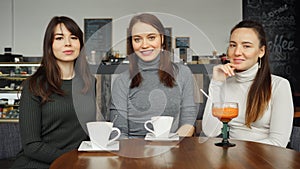 Three women girlfriends with beverages in a cafe are talking