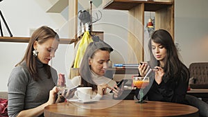 Three women girlfriends in a cafe are browsing their mobile phones. Friendly meeting in the cafe