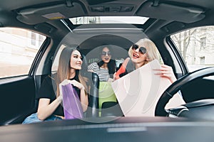 Three women have fun in the car after shoping and demonstrate new buy shoes