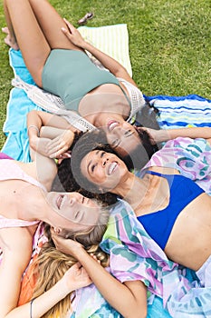 Three women are lying on a blanket, laughing together in an outdoor setting