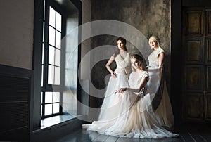 Three women near window wearing wedding dresses