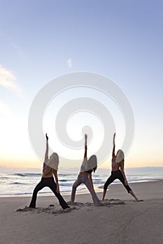 Three Women Practicing Yoga on Beach At Sunrise