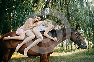 Three women are riding a horse next to tree