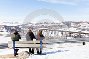Three women sitting on park bench in winter time.