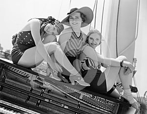 Three women sitting on top of a piano photo