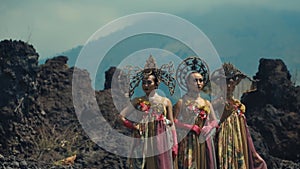 Three women in traditional attire with ornate headdresses standing before a mountainous backdrop