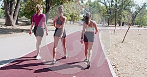 Three women walking in a park on a sunny day, showcasing fitness and friendship.