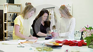 Three women in the workshop at the garment factory. They look at the colored fabrics for a new dress and look for