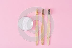 Three wooden bamboo toothbrushes and baking soda powder in glass jar on a pink background.  Teeth health and keep mouth concept