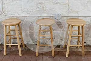 Three wooden barstools against a concrete cement wall in a basement