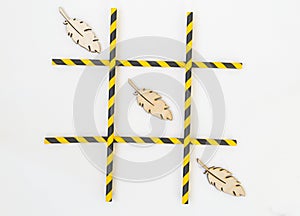 Three wooden bird feathers are lined up in a grid tic-tac-toe game on a white background. The grid consists of colored tubes from