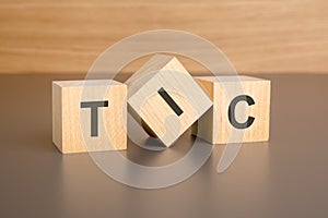 three wooden blocks on a brown background, with the abbreviation TIC