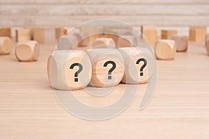 three wooden blocks with question marks over a brown background with copy space