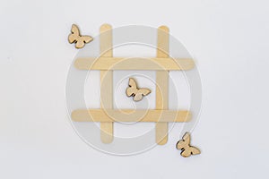 Three wooden butterflies lie in a row in the game of tic-tac-toe, in a grid on a white background. Concept summer