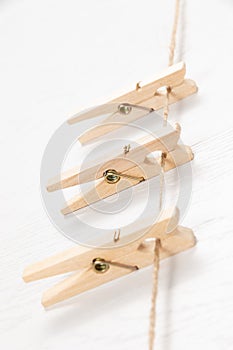 Three wooden clothespins with a metal spring hang on a rope on a white background.