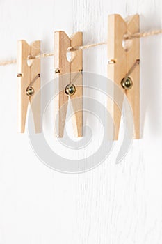 Three wooden clothespins with a metal spring hang on a rope on a white background