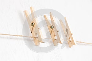 Three wooden clothespins with a metal spring hang on a rope on a white background