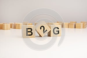 three wooden cubes with B2G symbols on them. white background. in the background there are many wooden blocks of