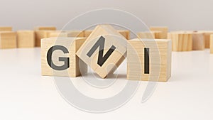 three wooden cubes with GNI symbols on them. white background. in the background there are many wooden blocks of