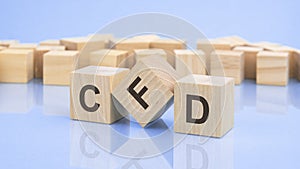 three wooden cubes with the letters CFD on the bright surface of a pale lilac table. the inscription on the cubes is