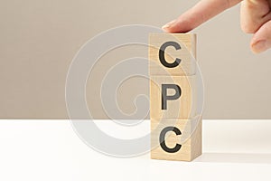 three wooden cubes with the letters CPC on the bright surface of a white table