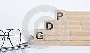 Three wooden cubes with letters GDP on the white table with keyboard and glasses