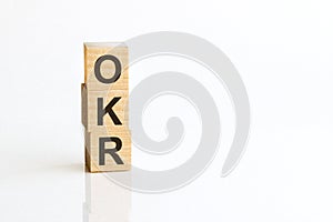 Three wooden cubes with letters OKR - Objectives and Key Results, on white table, more in background, space for text in right down