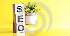 Three wooden cubes with letters - SEO - Search engine optimization, on yellow table, space for text in right. Front view concepts