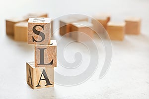 Three wooden cubes with letters SLA means Service Level Agreement, on white table, more in background, space for text in right
