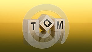 Three wooden cubes with the letters TQM on the bright yellow surface. the inscription on the cubes is reflected from the