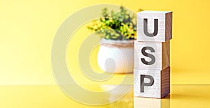 Three wooden cubes with letters - USP - on yellow table, front view concepts, flower in the background