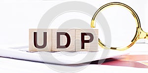 Three wooden cubes with the text UDP User Datagram Protocol stand on a white calculator near a magnifying glass. Business concept