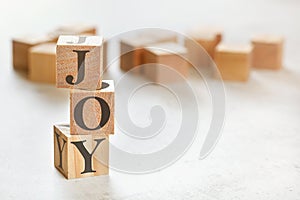 Three wooden cubes with word JOY, on white table, more in background, space for text in right down corner