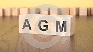 three wooden cubes on a yellow background, with the abbreviation AGM - Annual General Meeting