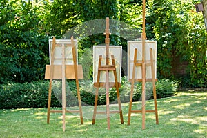 Three wooden easels with paintings standing on a green lawn in a garden or park in a concept of art and nature.