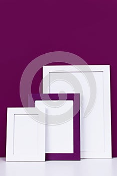 Three wooden empty frames for a photo on a white shelf on a background of a bright purple red wall. Blank paper frames